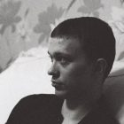 A man leans on a sofa, deep in thought, captured in striking black and white.