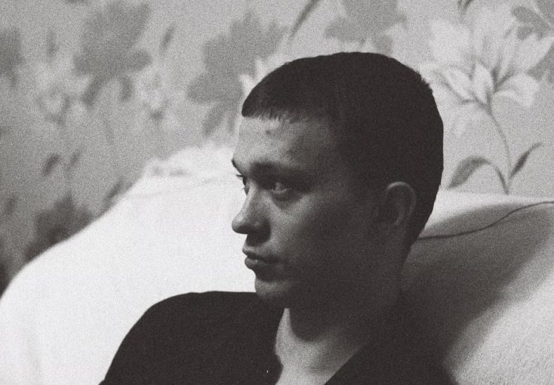 A man leans on a sofa, deep in thought, captured in striking black and white.